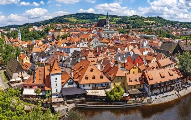 Panoramablick auf eine Altstadt mit Fluss und Hügeln im Hintergrund.