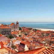 Blick auf historische Stadt mit roten Dächern und Küstenlinie im Hintergrund bei klarem Himmel.