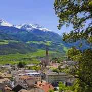 Stadtansicht mit Kirche vor schneebedeckten Bergen bei klarem Himmel.