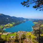 Blick auf einen klaren blauen See inmitten grüner Berge und Dörfer.