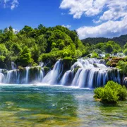 Wasserfall in grüner Landschaft unter blauem Himmel mit Wolken.