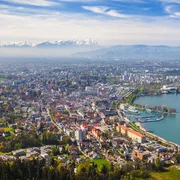 Panoramablick auf eine Stadt am See mit Alpen im Hintergrund.
