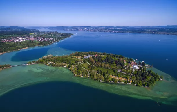 Luftaufnahme einer grünen Insel in einem blauen See bei klarem Himmel.