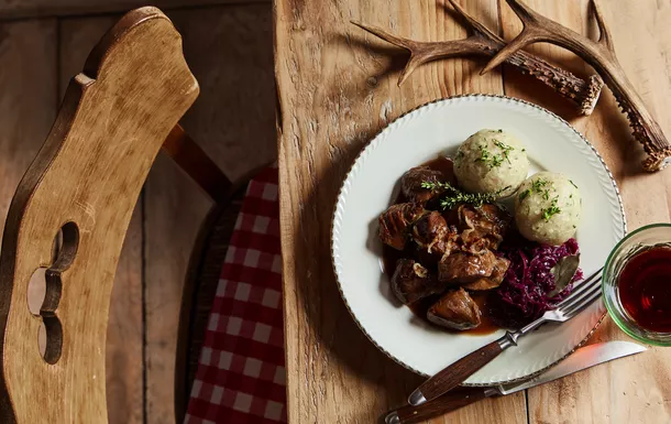 Teller mit Wildragout, Knödeln und Rotkraut auf rustikalem Holztisch.