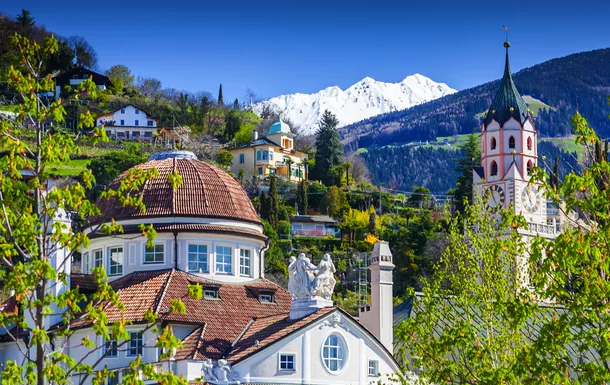 Alpenstadt mit Kirchturm und schneebedeckten Bergen im Hintergrund