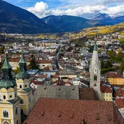 Kirchtürme und Gebäude einer Stadt vor Bergkulisse bei klarem Wetter.