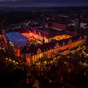 Luftaufnahme eines beleuchteten Weihnachtsmarkts in einer historischen Stadt bei Dämmerung.