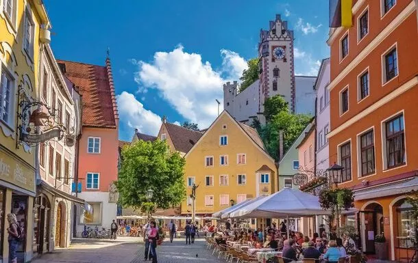 Lebendige Straßenszene mit bunten Häusern und Cafés bei sonnigem Wetter.